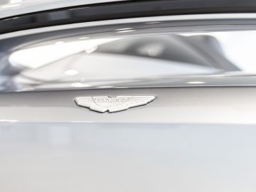 Close-up van een Aston Martin V12 Speedster-badge op een zilveren auto.
