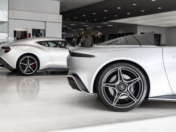 Twee Aston Martin V12 Speedsters tentoongesteld in een moderne showroom van een dealer.