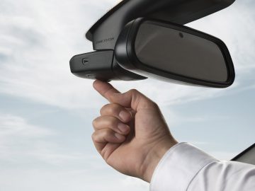 De hand van een persoon die handmatig de achteruitkijkspiegel van een auto verstelt om een Dashcam Nederland beter te positioneren.