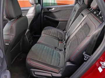 Binnenaanzicht van de voorstoelen en het dashboard van een Ford Kuga, met de nadruk op de zwarte bekleding met rode accenten.