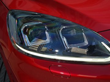 Close-up van de koplamp van een Ford Kuga op een rood voertuig.