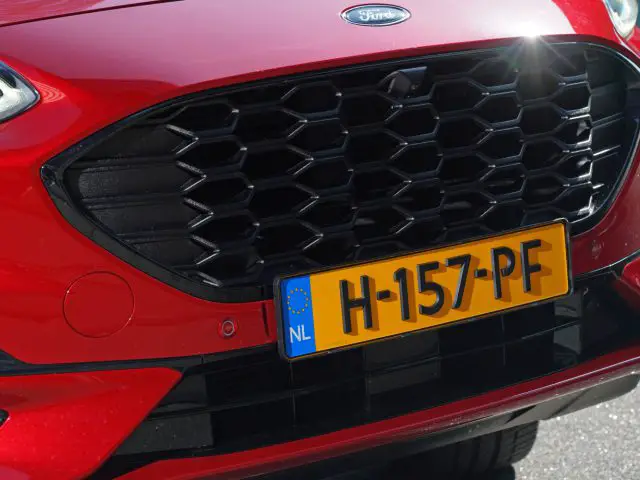 Close-up van de grille van een rode Ford Kuga en de Europese kentekenplaat.