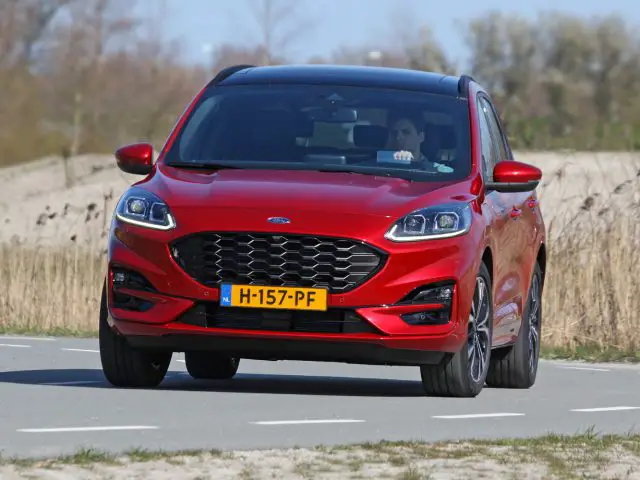 Rode Ford Kuga hatchback-auto die op een weg rijdt met een bestuurder zichtbaar binnenin.