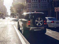 Een Land Rover Defender Commercial stopte bij een zonovergoten stedelijk kruispunt waar een bord 'Niet rechts afslaan' zichtbaar was.
