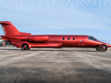 Een rode, op maat gemaakte limousine, ontworpen om op een vliegtuig te lijken, compleet met vleugels en staart, geparkeerd op een landingsbaan.