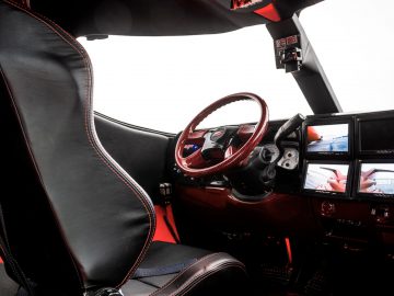 Binnenaanzicht van een moderne limousine met een zwart-rode racestoel, een rood stuur en een dashboard met meerdere schermen.