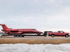 Een rode pick-up die een gedemonteerde limojet op een dieplader op een landingsbaan sleept.