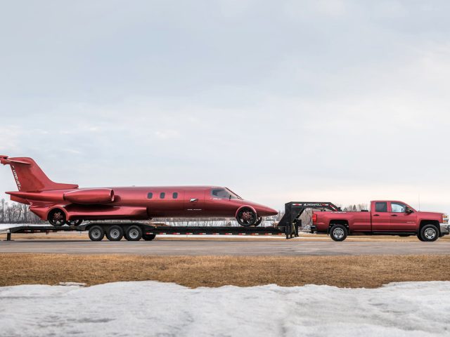 Een rode pick-up die een gedemonteerde limojet op een dieplader op een landingsbaan sleept.