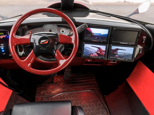 Binnenaanzicht van een op maat gemaakt limousine-dashboard met rode accenten en meerdere displays.