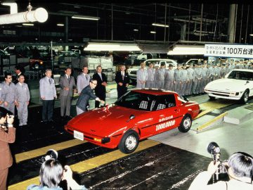 Werknemers en journalisten verzamelen zich rond een mijlpaal Mazda RX-7-productieauto tijdens een fabrieksfeest.