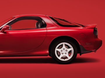Mazda RX-7 sportwagen tegen een bijpassende rode achtergrond, profielweergave.