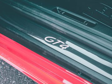 Close-up van de dorpel van een Porsche 718 Cayman GT4 met een "gt4"-logo op een koolstofvezeltextuur.
