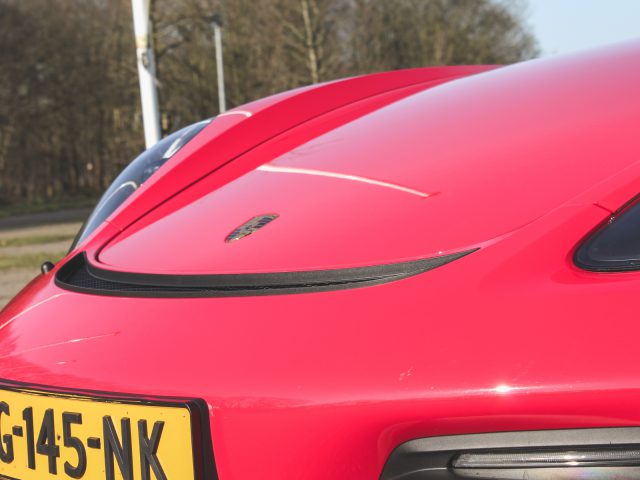 Close-up van een rood voertuig met de achterkant met het Porsche 718 Cayman GT4-embleem, geparkeerd langs de weg.