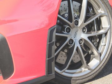 Close-up van het voorwiel van een rode Porsche 718 Cayman GT4 met remklauw met meerdere zuigers en geboorde rotoren.