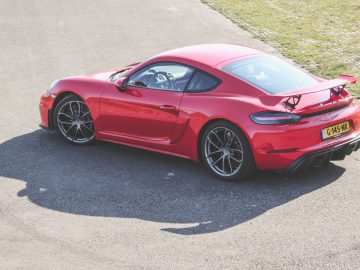 Rode Porsche 718 Cayman GT4 geparkeerd op een asfaltweg.