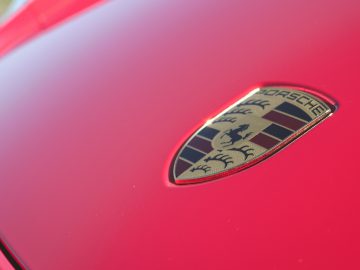 Close-up van een rode Porsche 718 Cayman GT4-motorkap met het embleem in focus.
