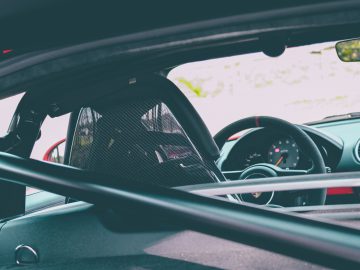 Binnenaanzicht van een Porsche 718 Cayman GT4 vanaf de achterbank, met het dashboard, het stuur en de achteruitkijkspiegel.