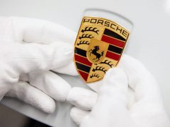 Handen in witte handschoenen met een Porsche-embleem.