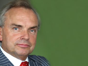 Portret van een man van middelbare leeftijd in een pak met een gestreepte stropdas tegen de achtergrond van een infrastructuur.