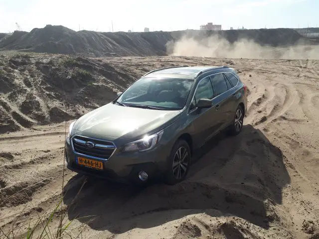Een Subaru Outback die vastzat in het zand met ingegraven wielen en stof achter zich aan.