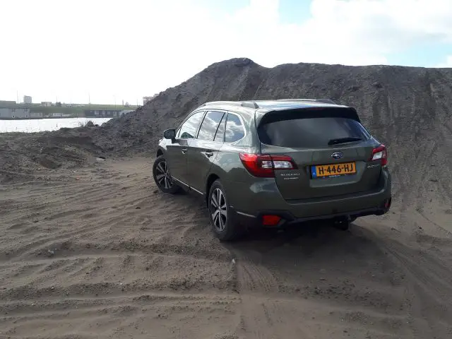 Een groene Subaru Outback geparkeerd op een zandgebied met stapels aarde op de achtergrond.