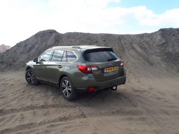 Een Subaru Outback geparkeerd op zanderig terrein met hopen vuil op de achtergrond.