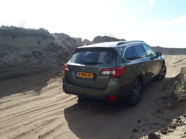 Een Subaru Outback die door een zanderig terrein navigeert.