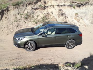 Een groene Subaru Outback geparkeerd op een zandhelling vlakbij een geërodeerde heuvel.