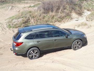 Een groene Subaru Outback geparkeerd op zanderig terrein.