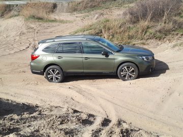 Een groene Subaru Outback zit offroad vast in het zand.