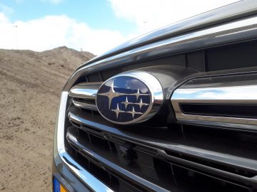 Close-up van de grille van een Subaru Outback met een Subaru-logo met een blauwe lucht en een aardse achtergrond.