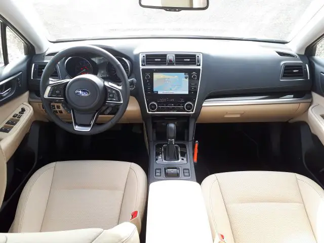 Binnenaanzicht van een Subaru Outback met een stuur met bedieningselementen, een touchscreen-infotainmentsysteem en een tweekleurig dashboard met beige stoelen.