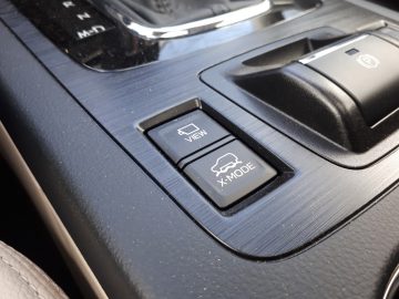 Close-up van het auto-interieur van een Subaru Outback met twee knoppen: één om het zicht van het voertuig aan te passen en de andere om de rijmodi te selecteren.