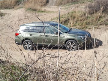 Een groene Subaru Outback geparkeerd op een zandpad te midden van droge vegetatie.