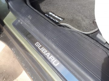 Close-up van een stoffige Subaru Outback-autoinstaplijst met het Subaru-logo zichtbaar.