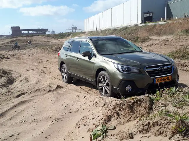 Subaru Outback vastgelopen op een zandpad met een fietser op de achtergrond.