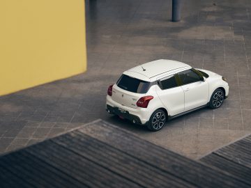 Witte Suzuki Swift Sport geparkeerd in een ruime, moderne garage met gele kolommen.