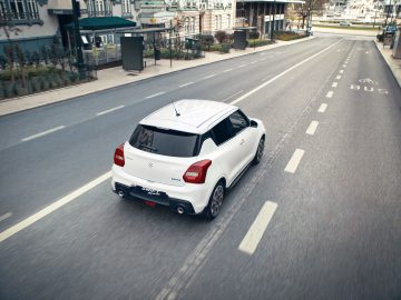Witte Suzuki Swift Sport hatchback rijdt op een aangewezen busbaan op een stedelijke weg.