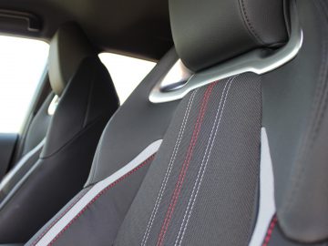 Zwart Toyota Corolla auto-interieur met een close-up van een sportieve lederen stoel met rode stiksels.