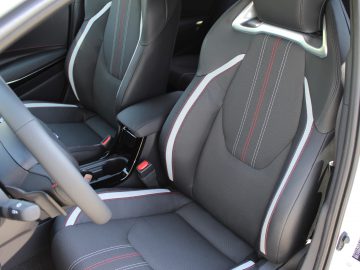 Het zwarte auto-interieur van Toyota Corolla met sportstoelen met rode stiksels.