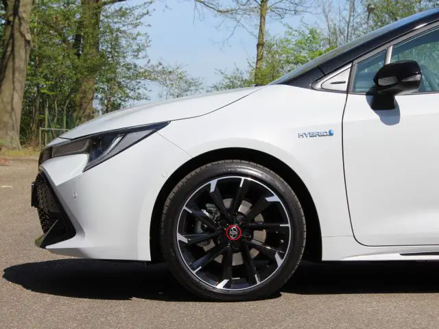 Witte Toyota Corolla hybride parkeergarage met focus op het voorwiel en de carrosserie aan de voorzijde.