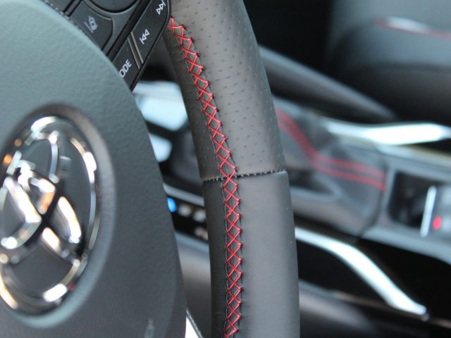 Close-up van het stuur van een Toyota Corolla met rood stiksel en een deel van het dashboard op de achtergrond.