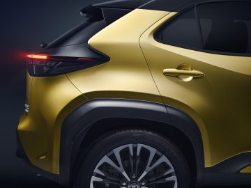 Achteraanzicht van een moderne gele Toyota Yaris Cross met led-achterlichten op een donkere achtergrond.