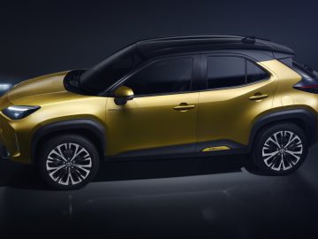 Een goudkleurige Toyota Yaris Cross tentoongesteld bij weinig licht, wat het strakke ontwerp en de lichtmetalen velgen benadrukt.
