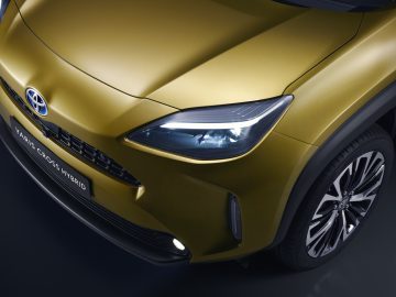 Close-up van een gouden Toyota Yaris Cross hybride voertuig met het koplamp- en grille-ontwerp.