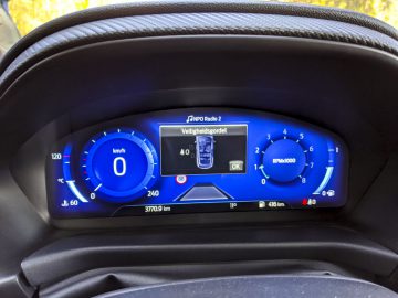 Digitaal dashboarddisplay van een Ford Puma met snelheidsmeter, brandstofmeter en informatie over het radiostation.
