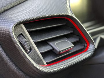 Ford Puma-autoventilatierooster met een rood accent op een getextureerd dashboard.