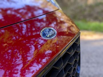 Close-up van een Ford Puma-embleem op de rode carrosserie van een auto met een wazige natuurlijke achtergrond.
