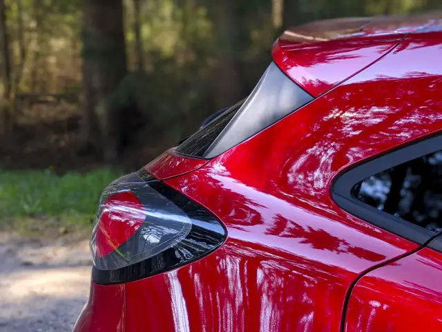 Close-up van het achterlicht en de achterspoiler van een rode Ford Puma met een wazige bosachtergrond.