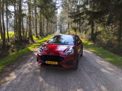 Rode Ford Puma geparkeerd op een onverharde weg omgeven door een bos op een zonnige dag.